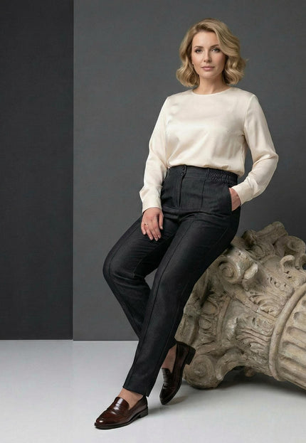 Официален дамски черен панталон с прав крачол за големи размери. Моделът е сниман в седнала поза върху декоративна колона, подчертаваща елегантния силует.