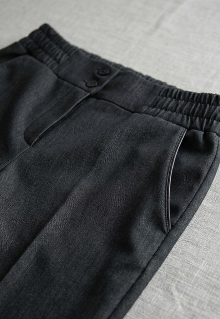 Детайл отблизо на официален дамски черен панталон, показващ еластичната талия, страничния джоб и закопчаването с две копчета.