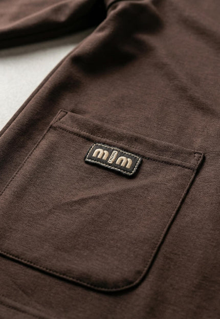 Детайл отблизо на официален дамски комплект в кафяв цвят, показващ преден джоб с декоративен етикет и качествената изработка на шевовете.