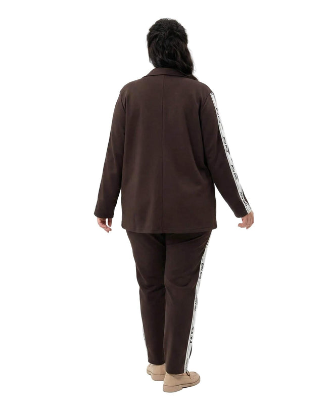 Официален дамски комплект от две части в кафяв цвят, изглед отзад. Сакото и панталонът се отличават с декоративни бели ленти с надписи по страничните ръбове.