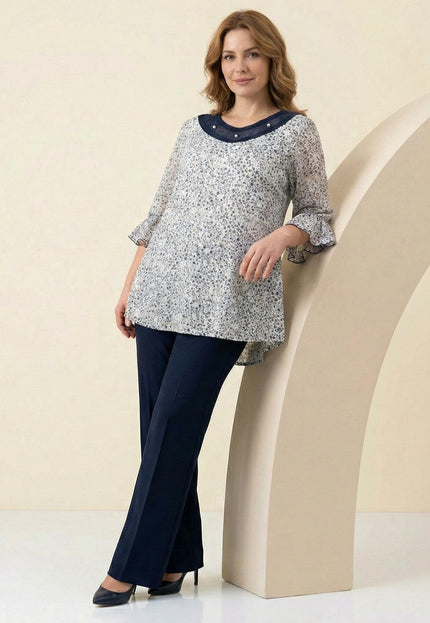 Дамска макси туника с флорален десен и перли на деколтето, заснета в цял ръст в комбинация с елегантен тъмен панталон.