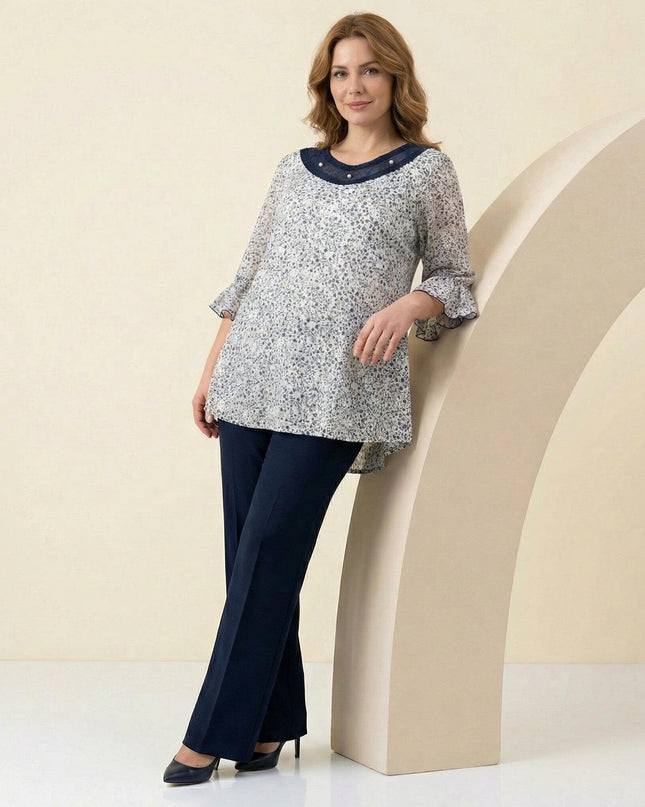 Дамска макси туника с флорален десен и перли на деколтето, заснета в цял ръст в комбинация с елегантен тъмен панталон.