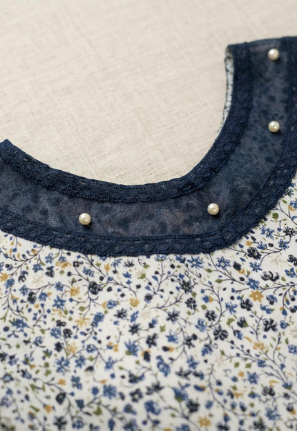 Детайл отблизо на деколтето на официална бяла макси туника на цветя, акцентирано с тъмносин тюл, дантелен кант и нежни перли.