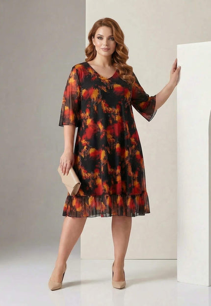 Цял ръст на модел, носещ официална черна макси рокля с шифон и абстрактен огнен принт, допълнена с волан на подгъва.