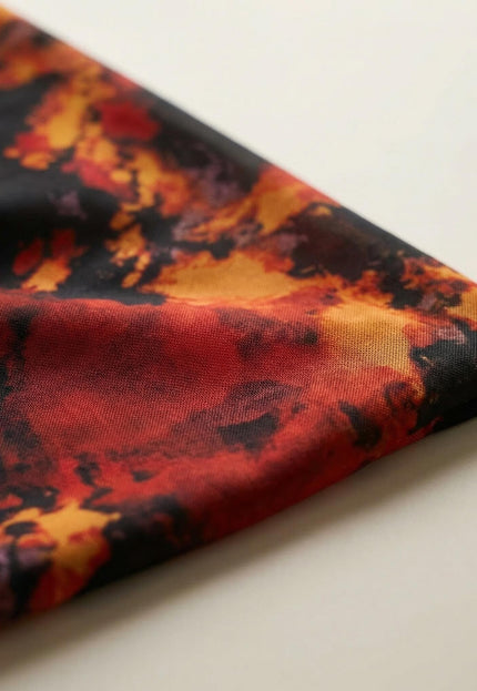 Детайл отблизо на материята на официална макси рокля, показващ ефирния шифон с абстрактен огнен принт на черен фон.