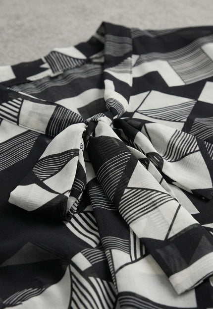 Детайл отблизо на официална макси туника с черно-бял геометричен принт и елегантна панделка около деколтето.