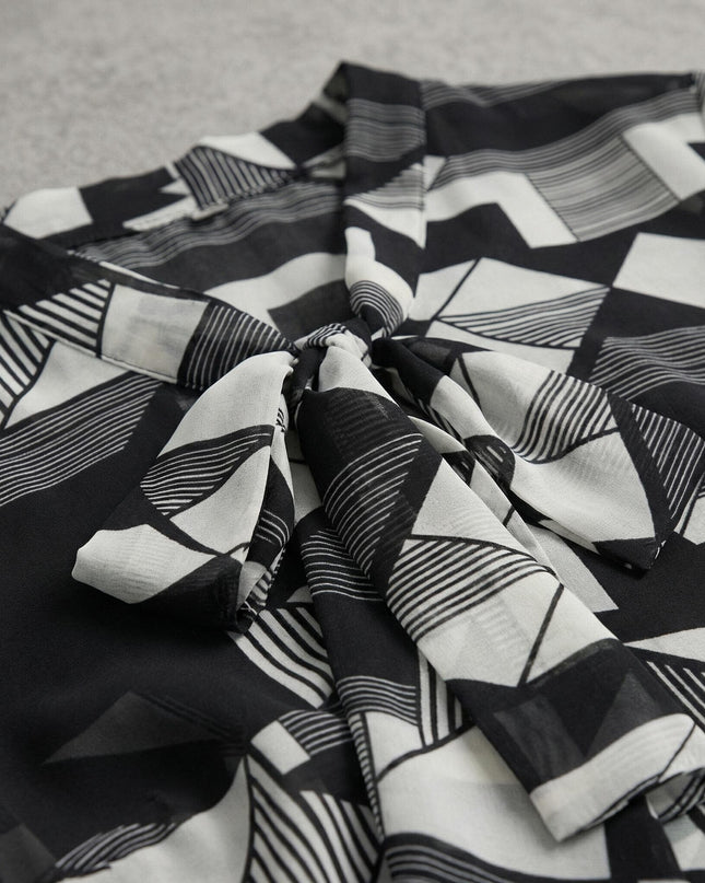 Детайл отблизо на официална макси туника с черно-бял геометричен принт и елегантна панделка около деколтето.