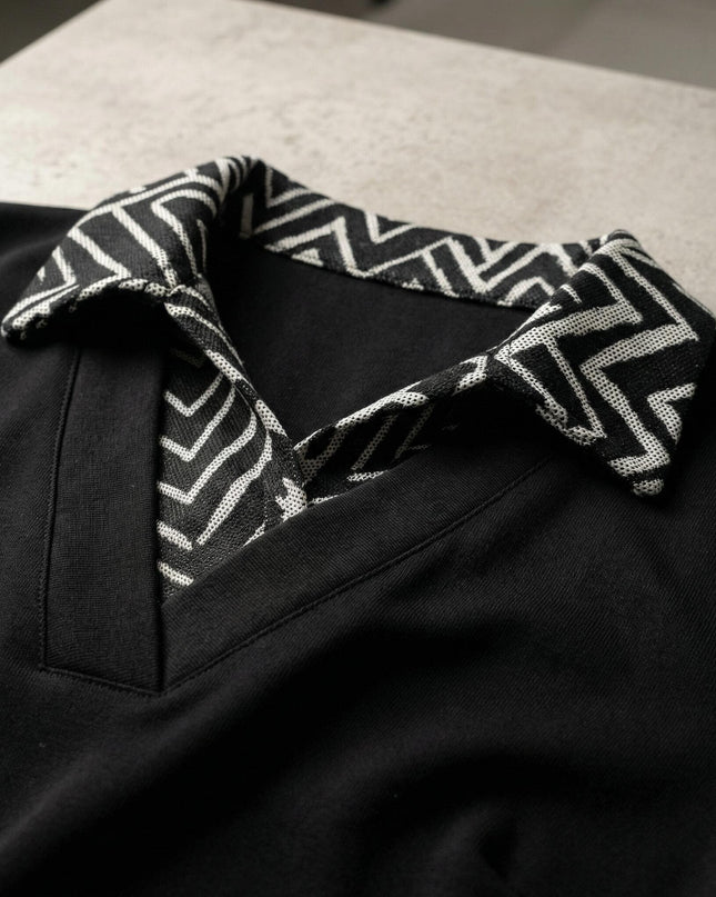 Детайл отблизо на официална черна туника, показващ стилната яка с черно-бял геометричен десен и V-образно деколте.