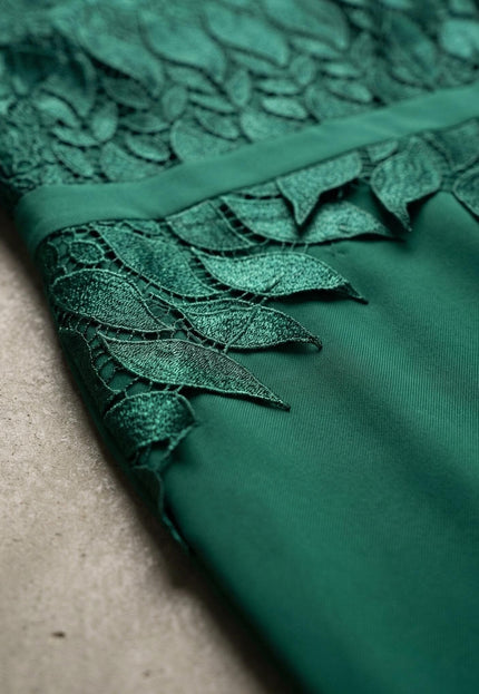 Детайлен кадър на официална макси рокля в масленозелен цвят, показващ отблизо изящната дантела с мотиви на листа и текстурата на плата.
