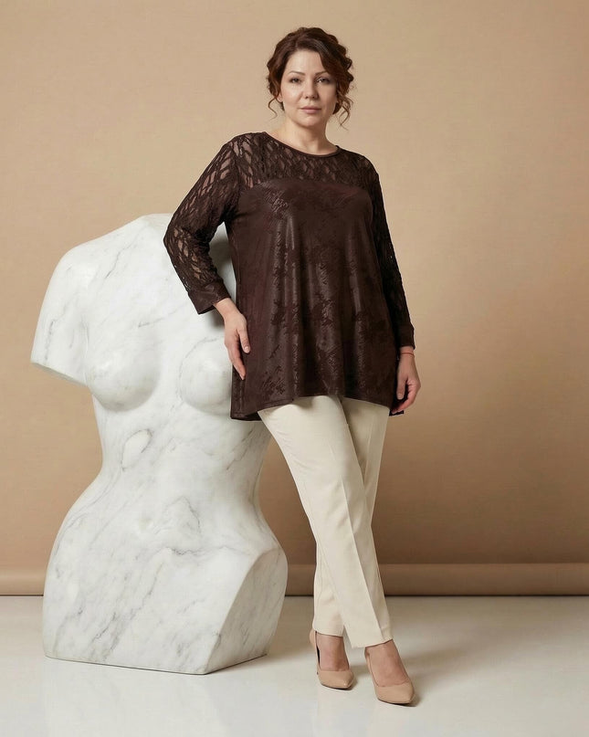 Елегантна официална макси туника в кафяво с прозрачни дантелени ръкави и платка. Снимка в цял ръст, където моделът позира до бяла скулптура.