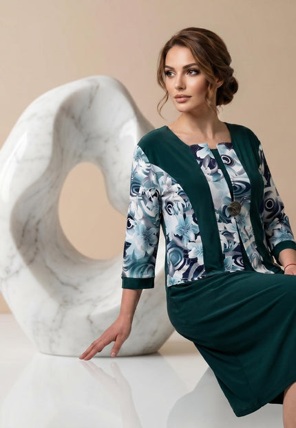 Официална масленозелена рокля големи размери с флорални мотиви. 3/4 кадър, показващ елегантния ефект от две части и декоративната брошка на деколтето.