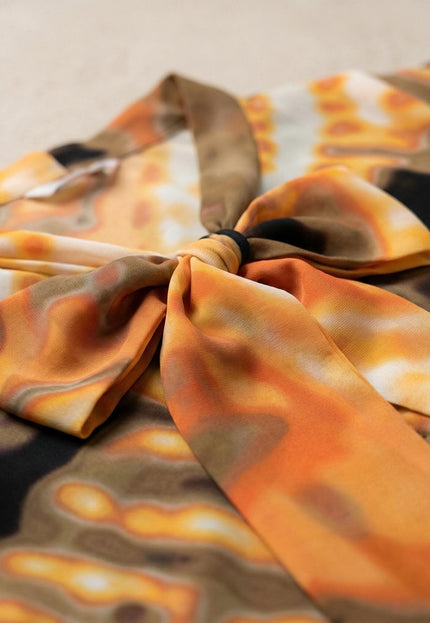 Детайлен кадър отблизо на деколте с елегантна панделка върху официална оранжева туника с абстрактен десен в земни тонове.