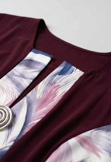 Детайл отблизо на официална макси рокля в бордо, показващ ефектен абстрактен принт на пера и декоративна спираловидна метална брошка.