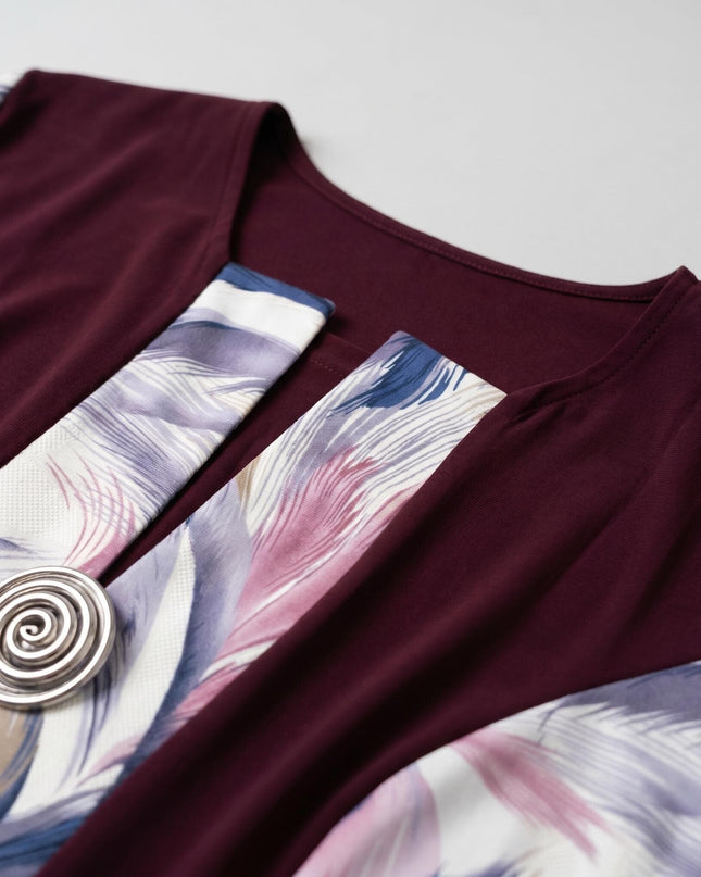 Детайл отблизо на официална макси рокля в бордо, показващ ефектен абстрактен принт на пера и декоративна спираловидна метална брошка.