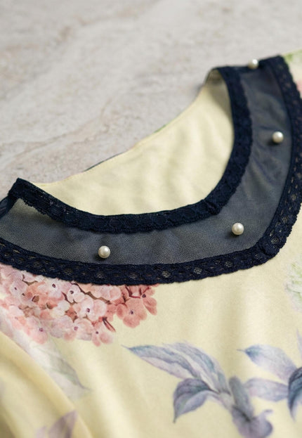 Детайл отблизо на деколтето на жълта макси туника на цветя. Акцентът е върху елегантната платка от тъмносин тюл с дантела и нежни бели перли.