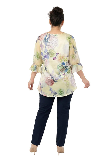 Официална разкроена макси туника на цветя в жълто, представена в гръб. Моделът показва свободната кройка и 7/8 ръкавите с нежни къдри в края.