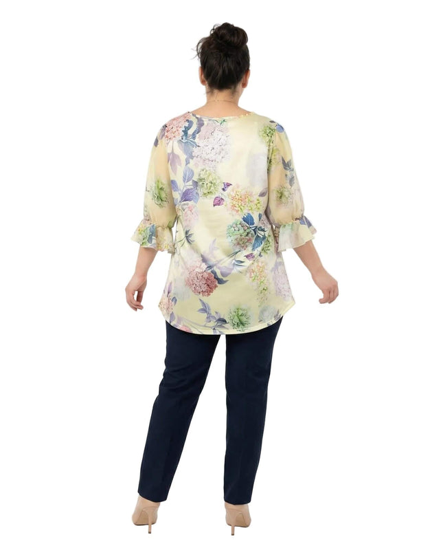 Официална разкроена макси туника на цветя в жълто, представена в гръб. Моделът показва свободната кройка и 7/8 ръкавите с нежни къдри в края.