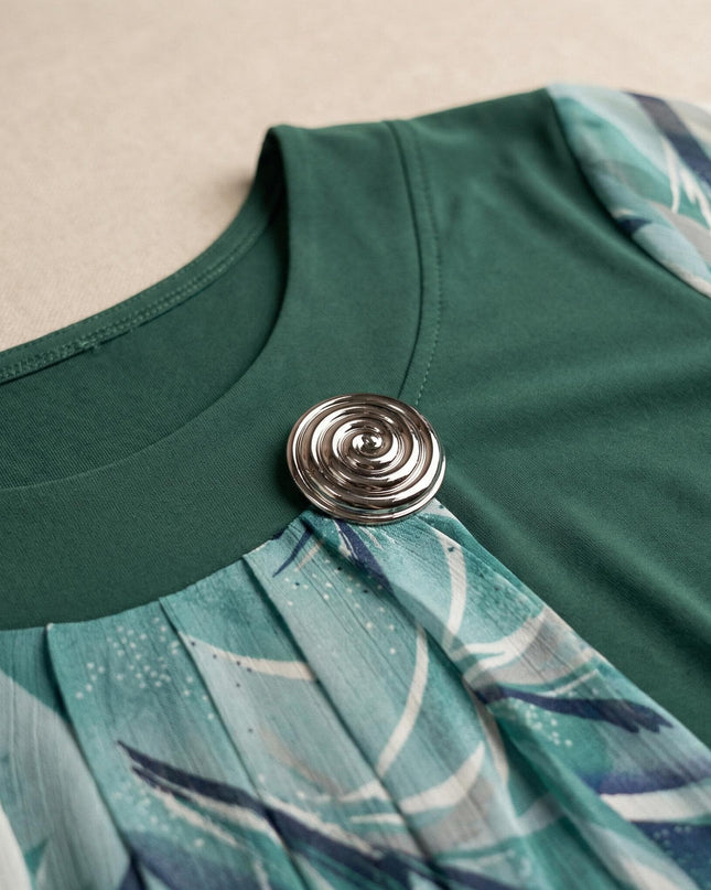 Детайлен кадър на деколтето на официална макси туника в масленозелено, акцентиращ върху елегантната сребриста брошка и набрания флорален шифон.