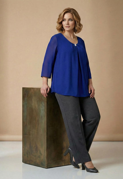 Официална разкроена туника от шифон в наситено кралскосин цвят с брошка на деколтето, показана в цял ръст върху модел, подпрян на декоративен куб.