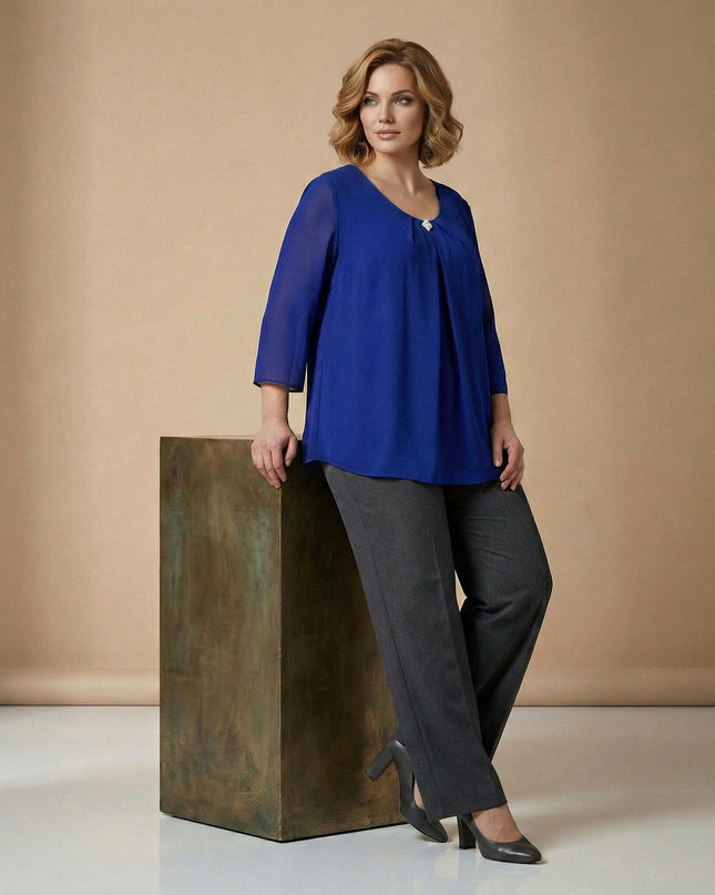 Официална разкроена туника от шифон в наситено кралскосин цвят с брошка на деколтето, показана в цял ръст върху модел, подпрян на декоративен куб.