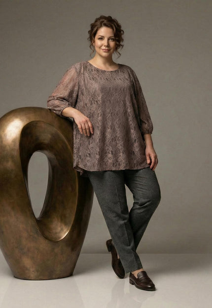 Елегантна разкроена туника с дантелен ефект и 3/4 ръкави, заснета в цял ръст до голяма бронзова скулптура.