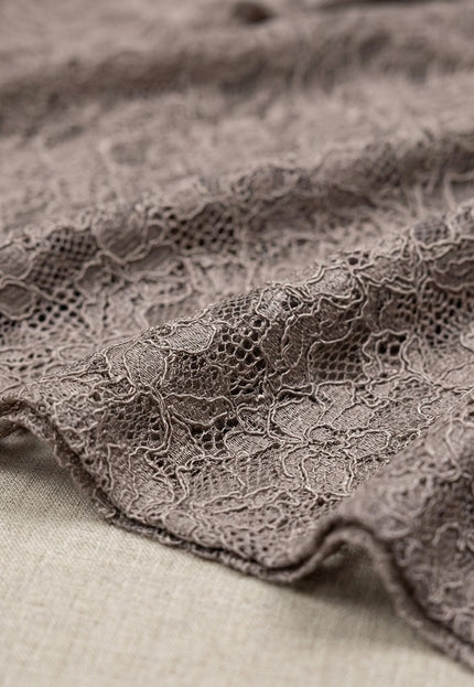 Детайл отблизо на материята на официална разкроена туника, показващ релефна дантелена текстура.