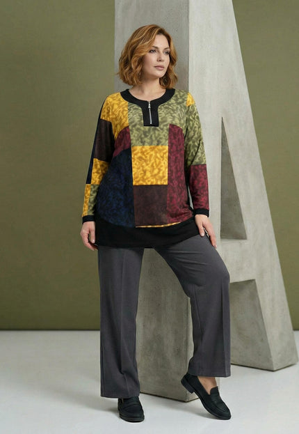 Елегантна шарена макси туника с пачуърк мотиви и цип на деколтето, показана в цял ръст върху модел до бетонен декор.