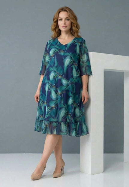 Официална шифонена рокля големи размери в синьо-зелени преливащи тонове, представена в цял ръст с V-образно деколте и волан на подгъва.