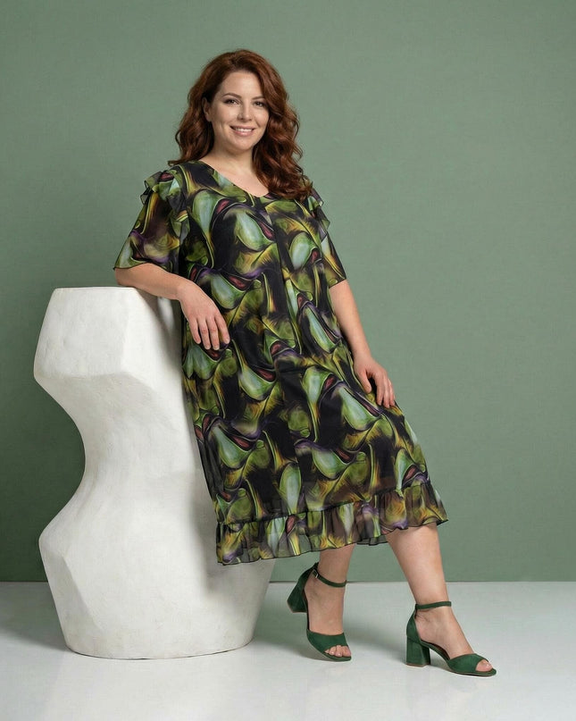 Официална шифонена рокля с пъстър десен и волани, представена върху модел в седнала позиция на зелен фон.