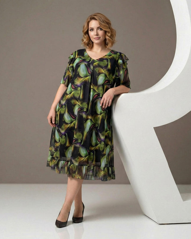 Официална шифонена рокля в пъстър десен с разкроена кройка и ефирни волани, представена върху модел в цял ръст до бял декор.