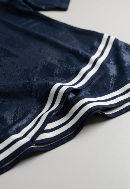Детайл отблизо на тъмносиня туника големи размери, показващ текстурираната еластична материя и черно-белия раиран кант по подгъва.