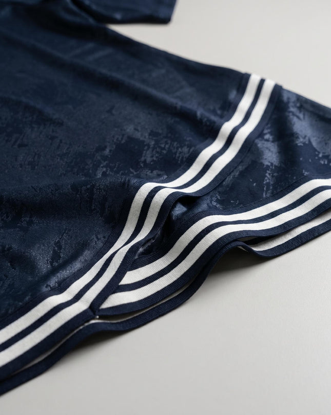 Детайл отблизо на тъмносиня туника големи размери, показващ текстурираната еластична материя и черно-белия раиран кант по подгъва.