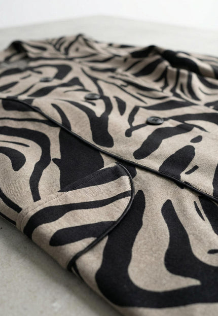 Детайлен кадър отблизо на официално дамско макси сако в бежово, показващ ефектния черно-бежов десен, закопчаването с копчета и джоба върху равна повърхност.