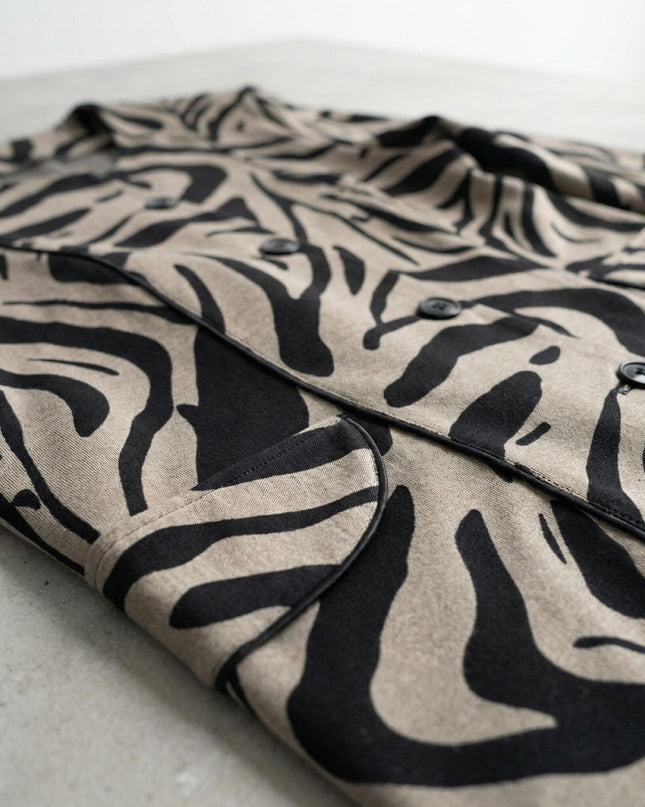 Детайлен кадър отблизо на официално дамско макси сако в бежово, показващ ефектния черно-бежов десен, закопчаването с копчета и джоба върху равна повърхност.