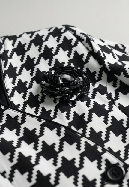 Детайлен кадър на официално дамско сако в пепит, показващ отблизо декоративната черна роза, яката с кант и текстурата на материята.