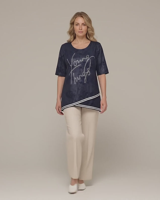 Видео представяне в студийна среда с неутрален фон, в което плюс сайз модел върви бавно към камерата, облечен с Официална тъмносиня туника големи размери с асиметрична кройка и камъчета