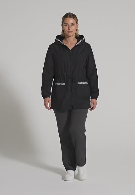 Видео в студийна среда, на което плюс размер модел върви бавно към камерата, носейки Черна разкроена макси ветровка с качулка и джобове