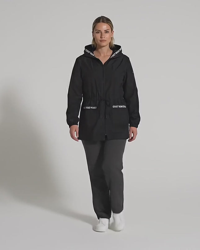 Видео в студийна среда, на което плюс размер модел върви бавно към камерата, носейки Черна разкроена макси ветровка с качулка и джобове