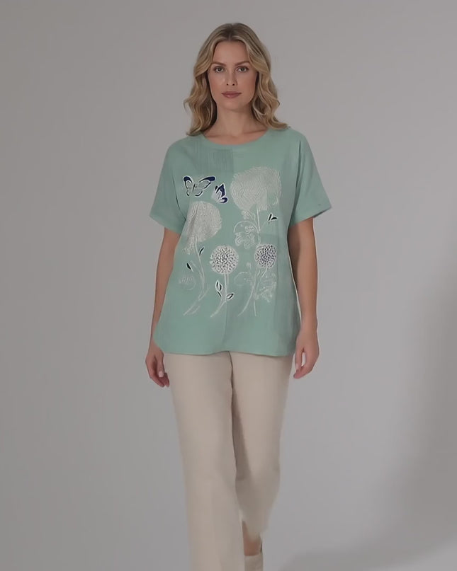 Студийно продуктово видео, показващо макси модел, който върви бавно към камерата и носи Дамска лятна макси туника в зелено с флорална апликация