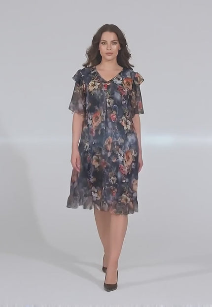 Студийно видео представяне на макси манекенка на неутрален фон, която върви бавно към камерата, облечена в Официална разкроена рокля от шифон на цветя с еластична подплата