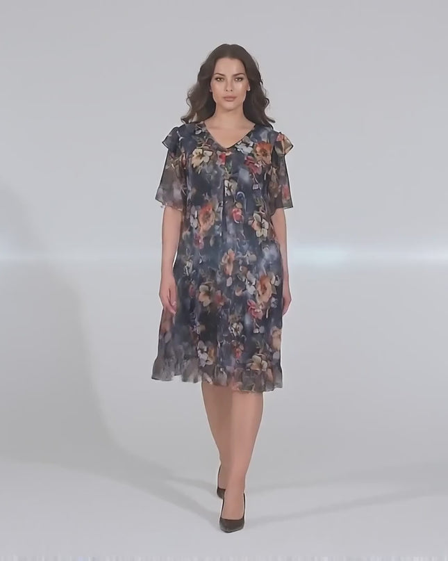 Студийно видео представяне на макси манекенка на неутрален фон, която върви бавно към камерата, облечена в Официална разкроена рокля от шифон на цветя с еластична подплата