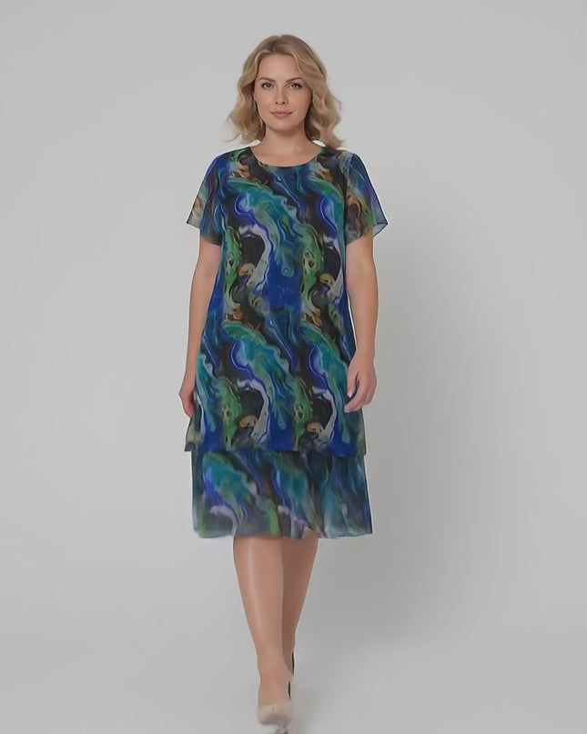 Плюс размер модел върви бавно към камерата в студийна среда на неутрален фон, носейки Официална шифонена рокля в преливащи тонове големи размери