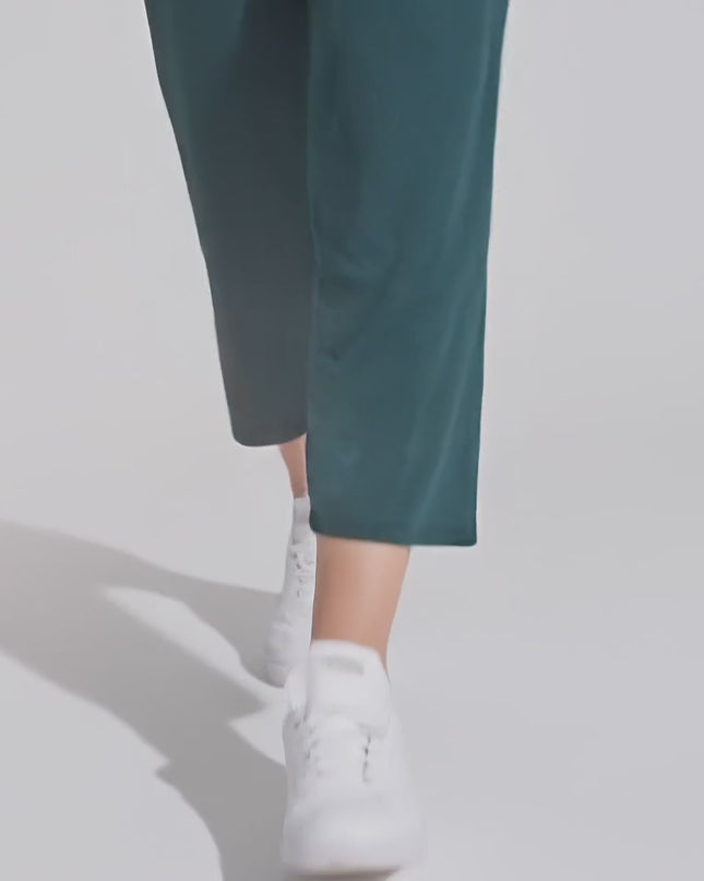 Плюс сайз модел, облечена с Еластичен тъмнозелен 7/8 панталон - Свободна кройка, върви бавно към камерата в студио с неутрален фон