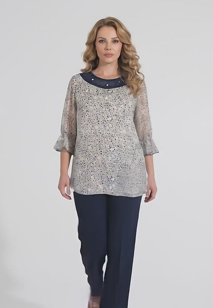 Видео в студийна среда, на което макси модел се разхожда бавно към камерата на неутрален фон, носейки Официална бяла макси туника на цветя с перли и тюл