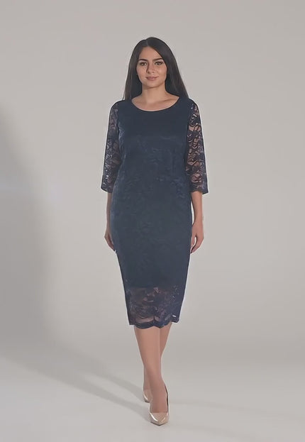 Макси модел, облечен в Официална дантелена рокля с 7/8 ръкав - Тъмносиня, върви бавно към камерата в студио с неутрален фон