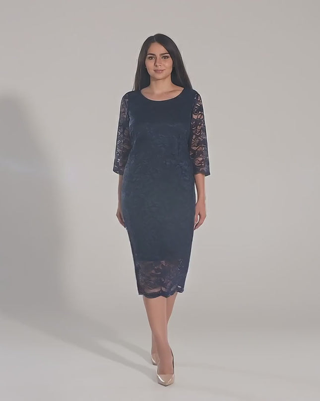 Макси модел, облечен в Официална дантелена рокля с 7/8 ръкав - Тъмносиня, върви бавно към камерата в студио с неутрален фон