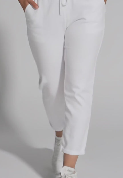 Плюс сайз модел в студийна среда върви бавно към камерата, облечен с Бели прави дамски панталони до глезена с ластик и връзки