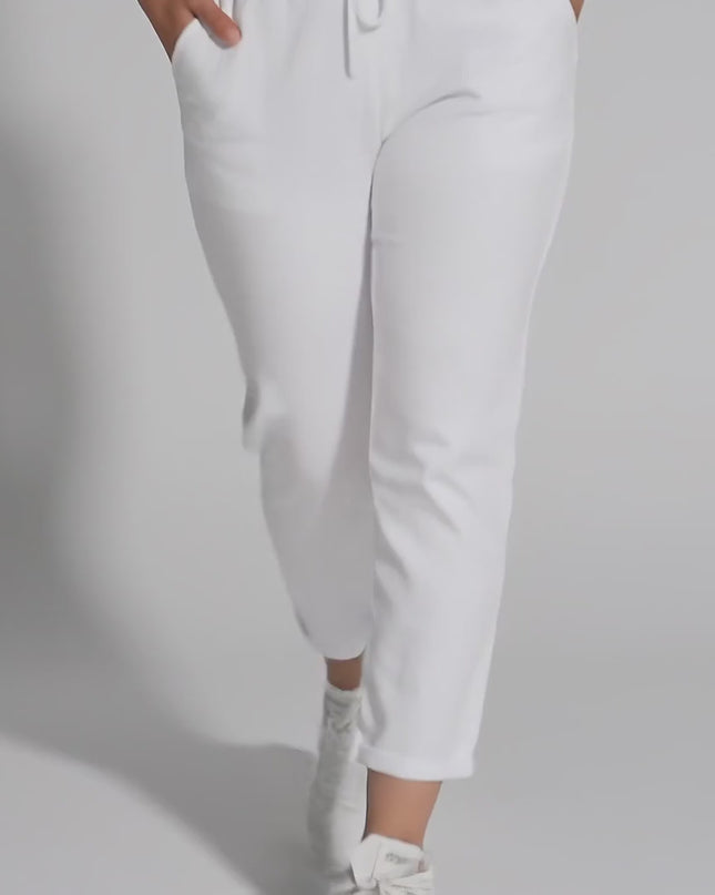 Плюс сайз модел в студийна среда върви бавно към камерата, облечен с Бели прави дамски панталони до глезена с ластик и връзки