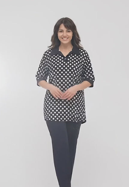 Видео заснето в студио на неутрален фон, показващо макси модел, който върви бавно към камерата, облечен в Официална черна макси туника на бели точки с якичка