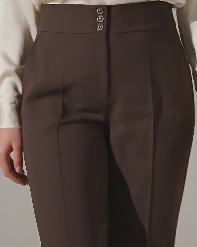 Плюс размер модел крачи бавно към камерата в студийна среда на неутрален фон, носейки Елегантен кафяв панталон с висока талия и копчета големи размери